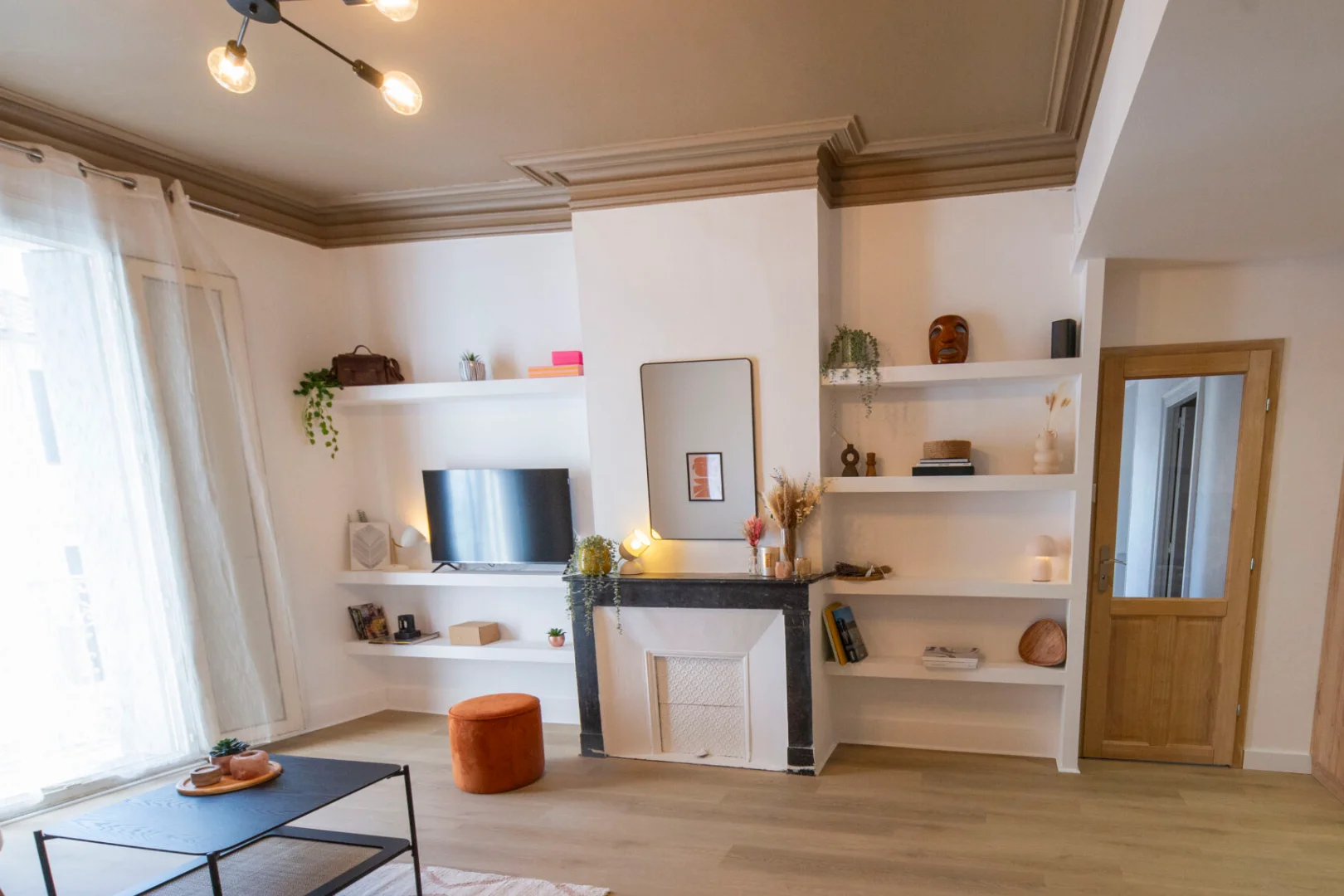 Salon d'un appartement haussmannien rénové à Montpellier, bibliothèque sur mesure autour de la cheminée en marbre, moulures et grandes fenêtres