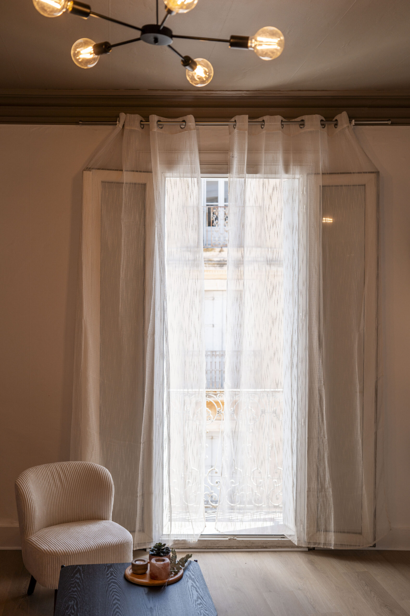 Fenêtre haute avec voilages, fauteuil bouclette et table basse dans le salon